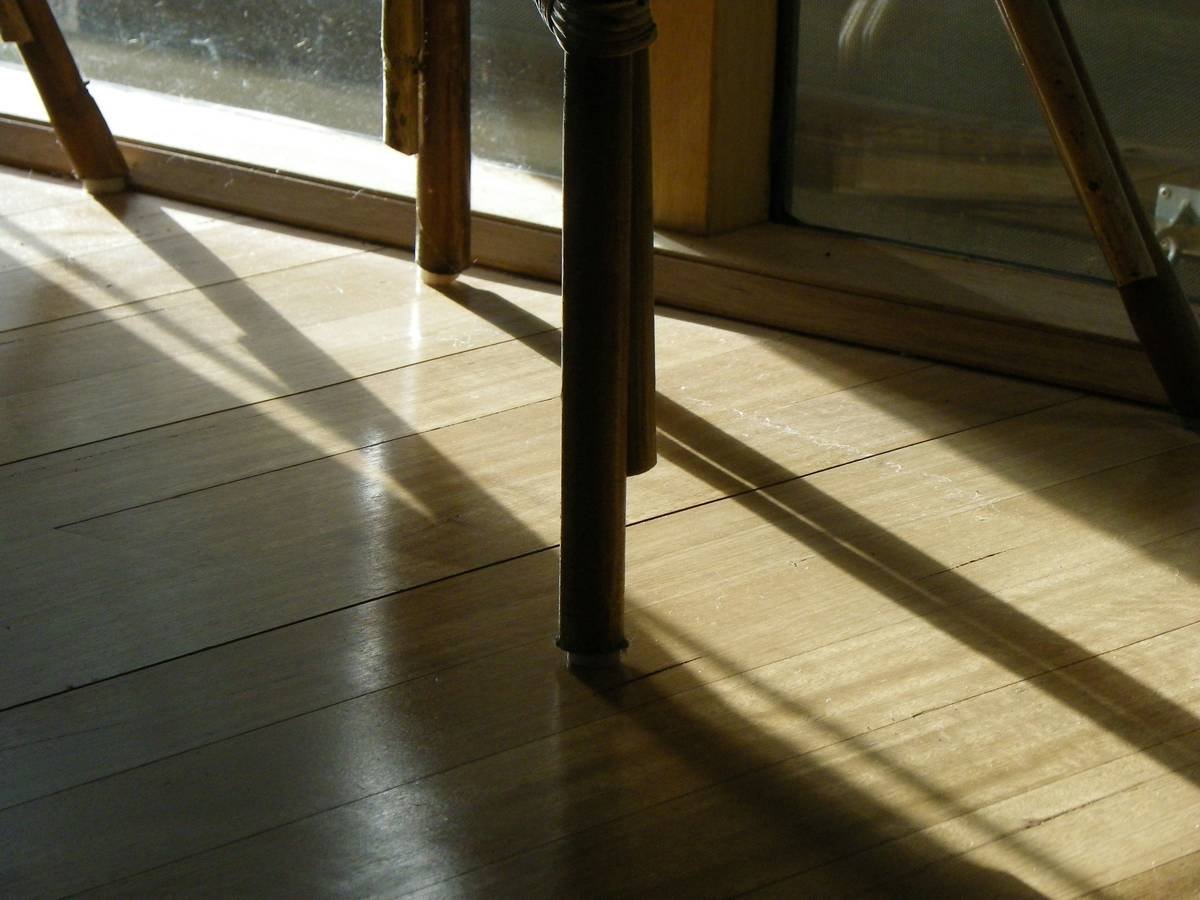 Close-up of scratched hardwood floor next to furniture coasters to protect floors